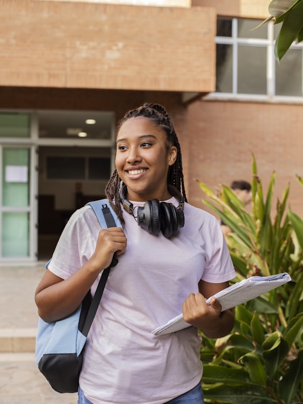 A smiling secondary school student carrying a backpack and notebooks