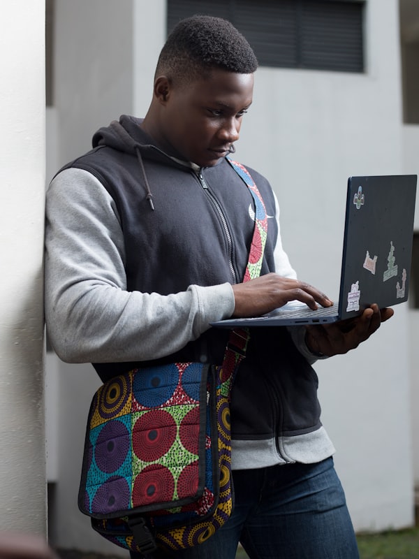 A student working on a laptop, an Ankara-print bag over his shoulder